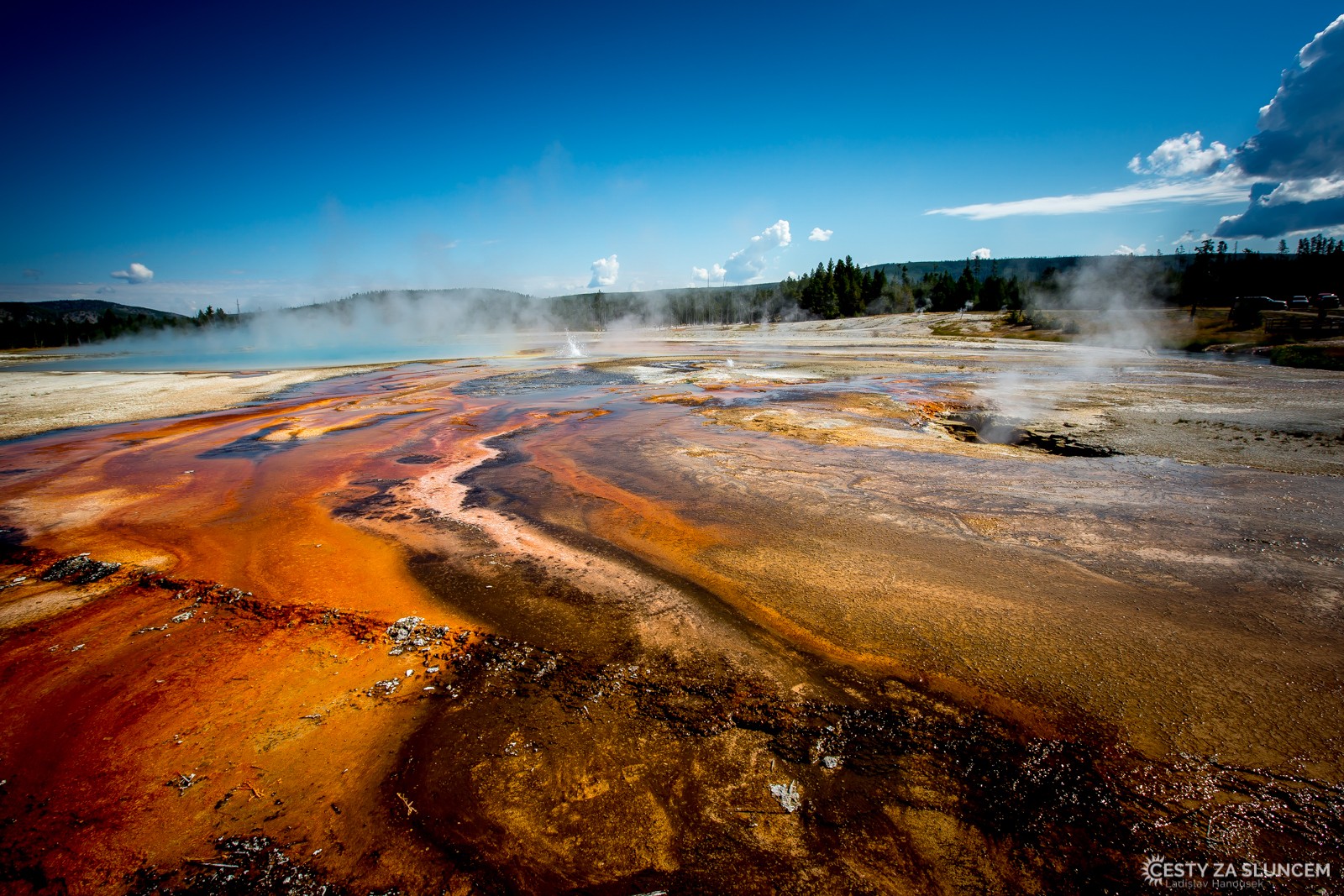 Oblast Midway Geyser Basin. Prameny, které napájejí jezírka, jsou stále aktivvní. Z vody stoupá syčící pára, barva jezírek je od sytě modré uprostřed až po hnědou na okrajích. - Ladislav Hanousek, Yellowstone NP